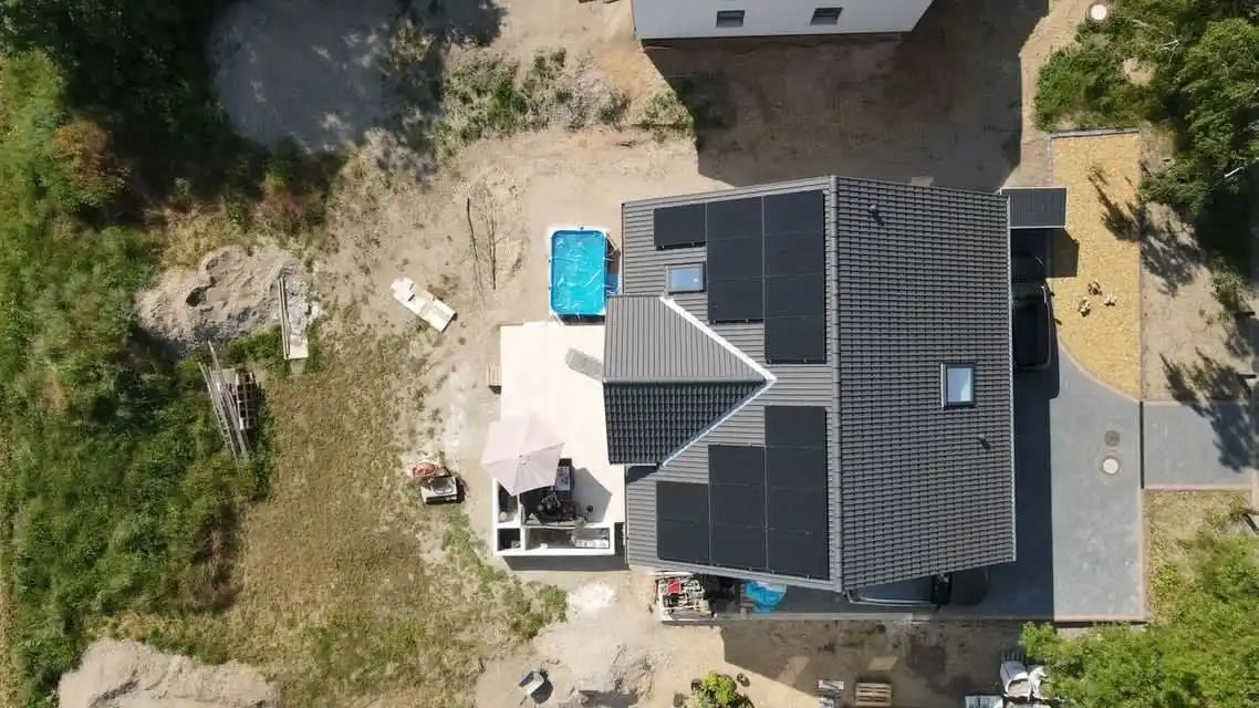 Modernes Haus mit dunkelgrauem Ziegeldach und Solarpanelen aus der Vogelperspektive.